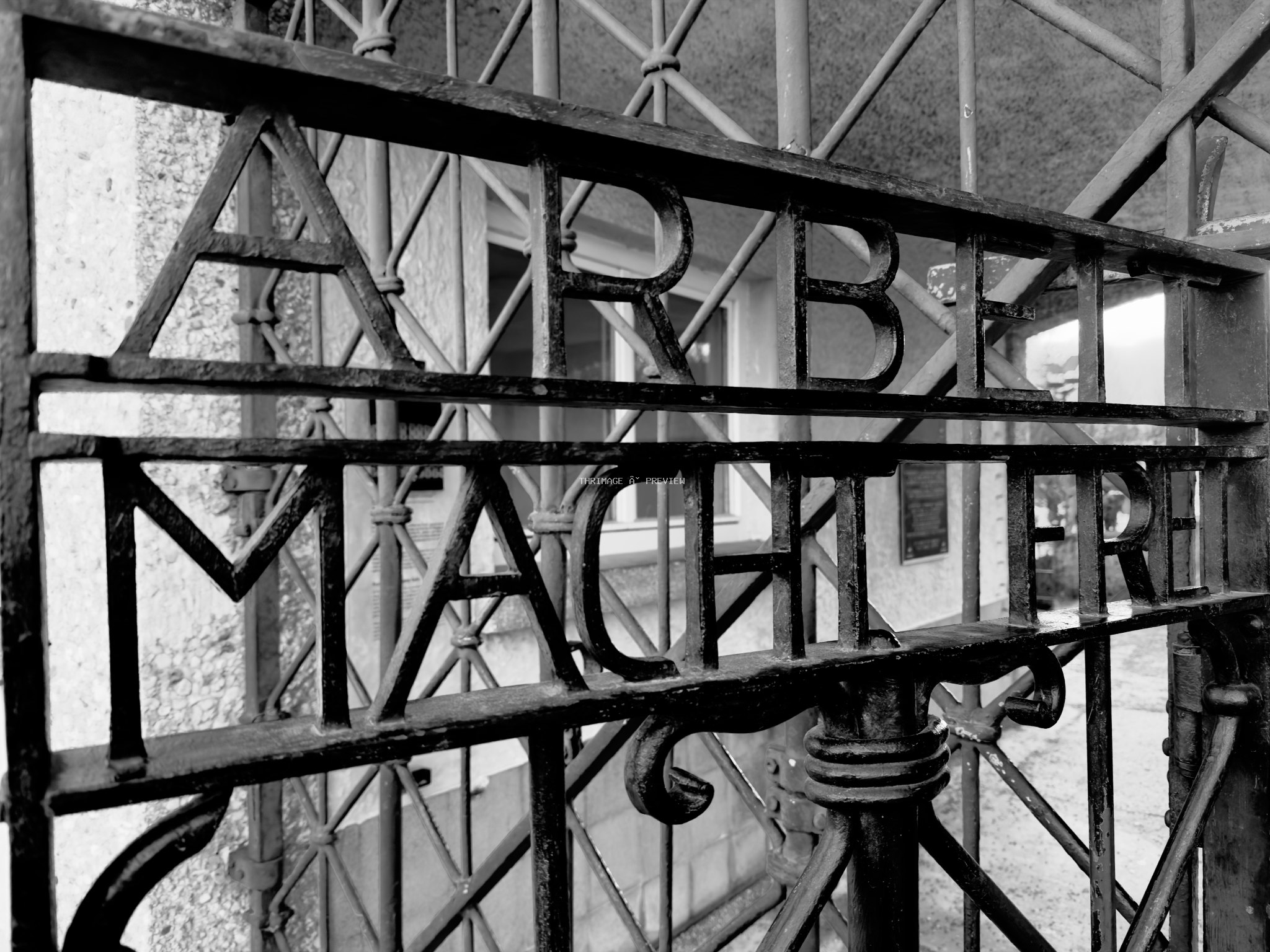 Close-up black-and-white view of the wrought-iron Arbeit Macht Frei gate at Dachau Memorial Site