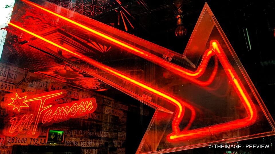 Red neon arrow and star sign glowing against a dark, graphic-covered interior.
