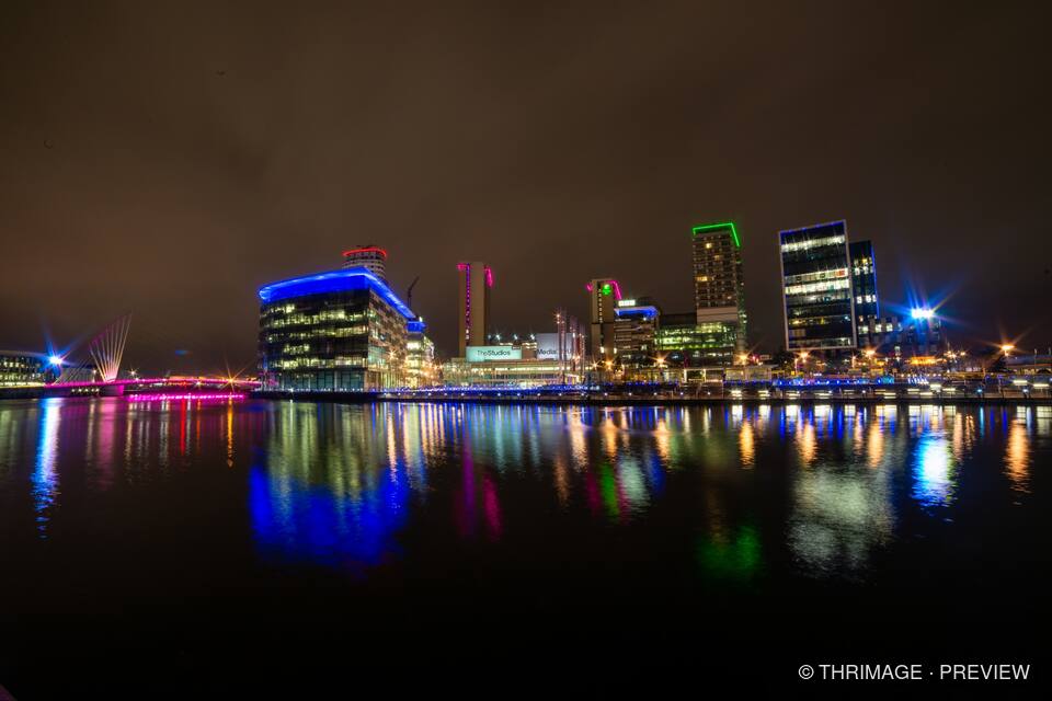 Illuminated MediaCity buildings and waterfront lights reflected in Salford Quays at night