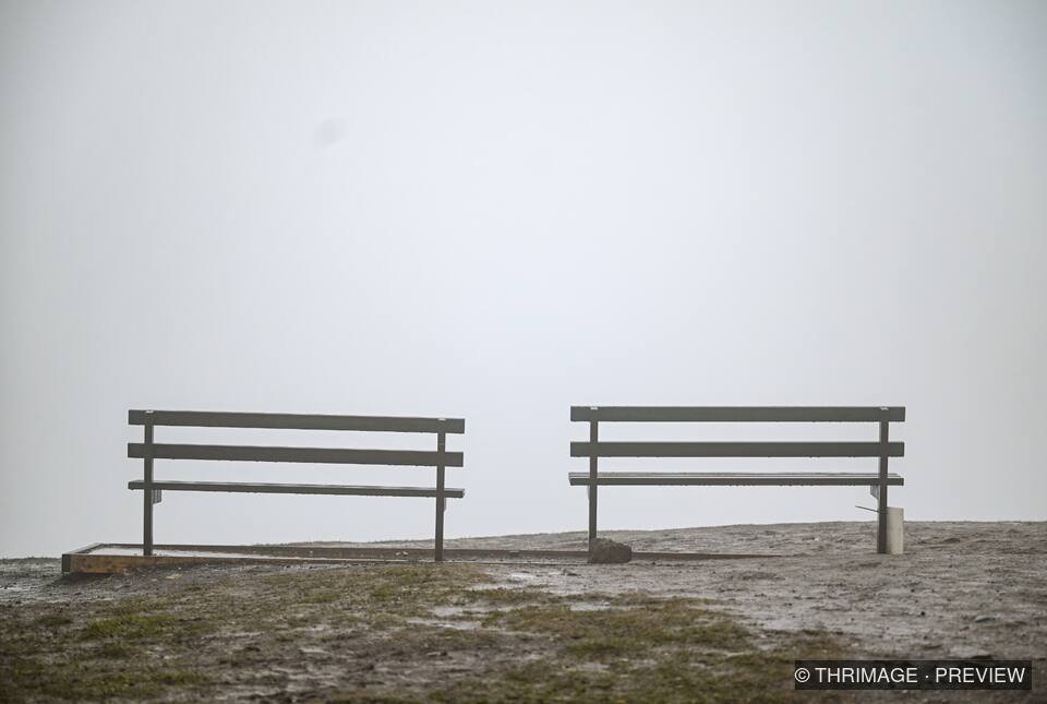 Two empty wooden benches on a wet, barren landscape fading into dense white mist.