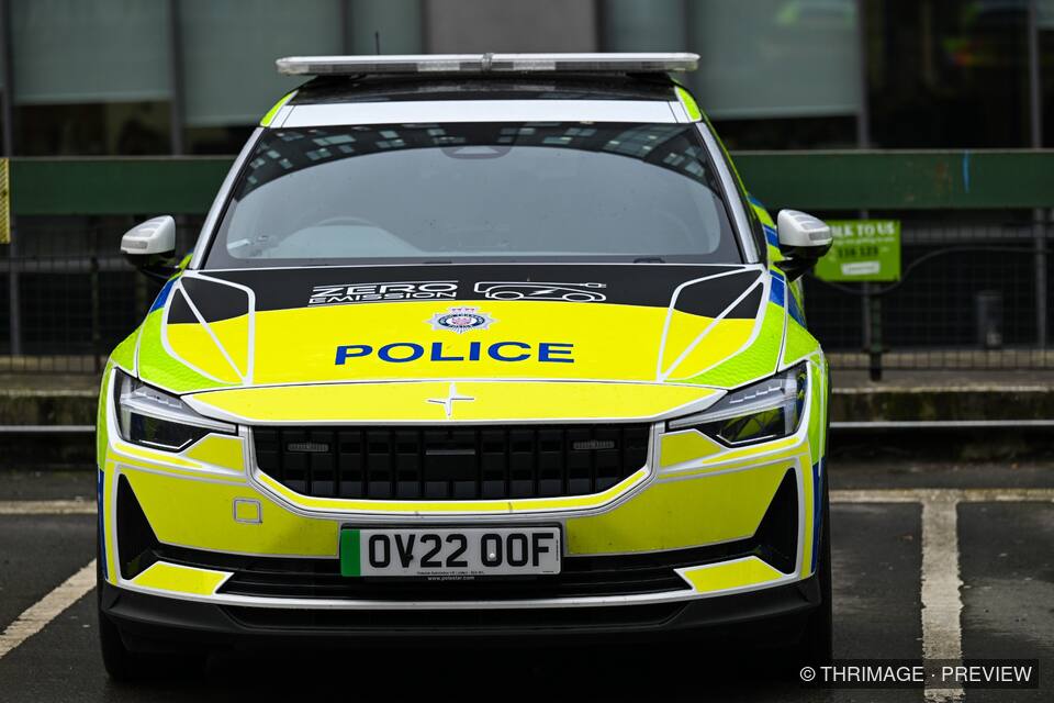 Front view of a marked British police car with yellow-and-blue livery parked outside a building.