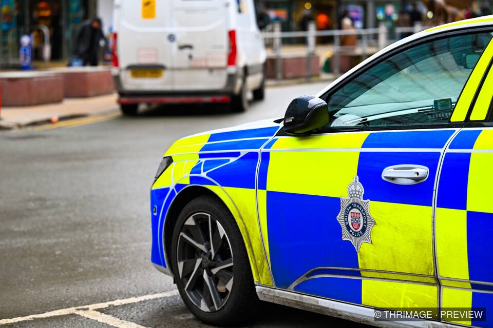 Close-up of a blue-and-yellow British Transport Police car beside an urban street, with a white van and blurred pedestrians behind it.