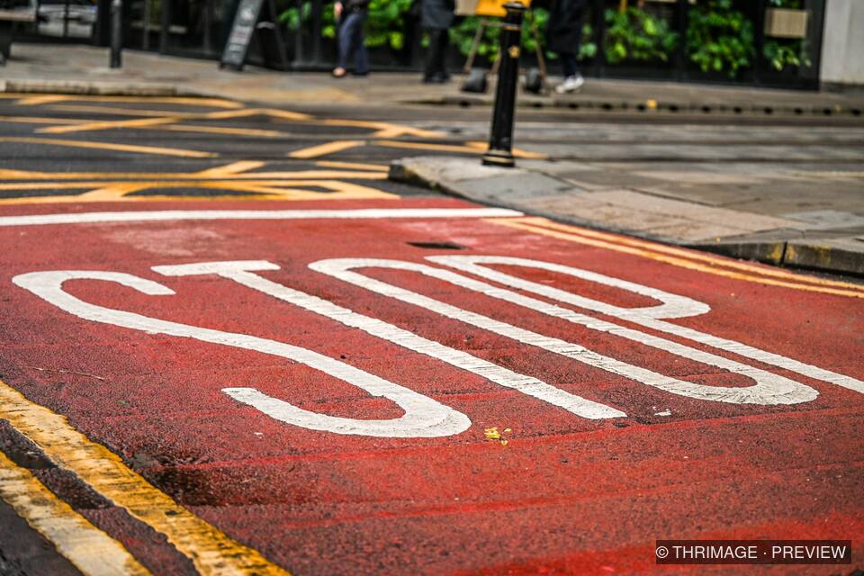 Large white STOP marking on a red road surface beside a sidewalk and yellow curb lines.