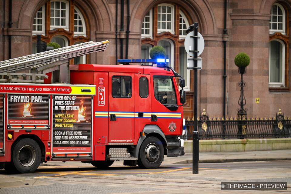 Red fire engine with an extended ladder parked outside a historic stone civic building
