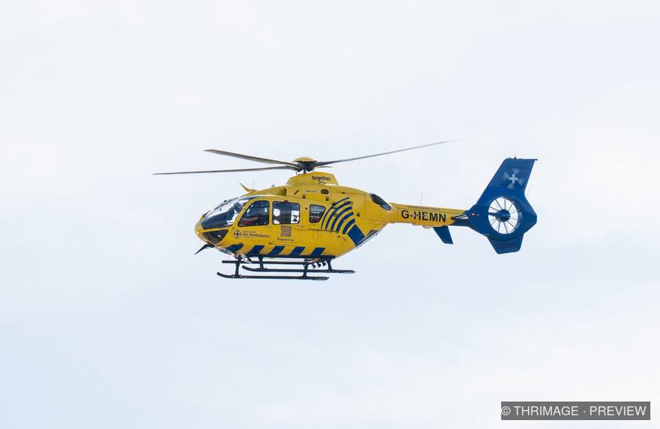 Yellow-and-blue air ambulance helicopter flying in profile against a pale sky