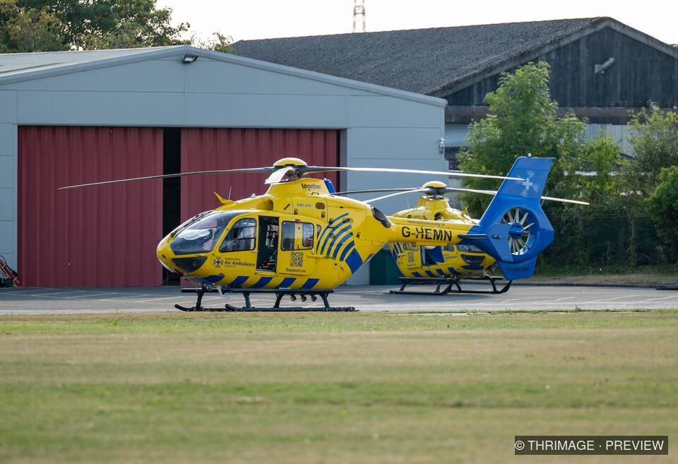 Two yellow-and-blue air ambulance helicopters parked outside a hangar.