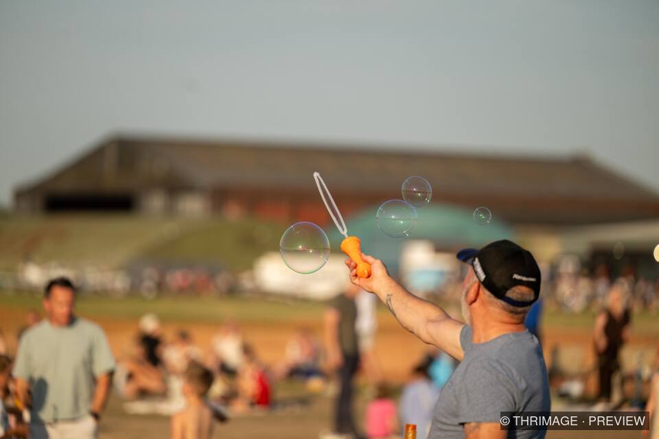 Man holding a bubble wand as soap bubbles float above an outdoor crowd.