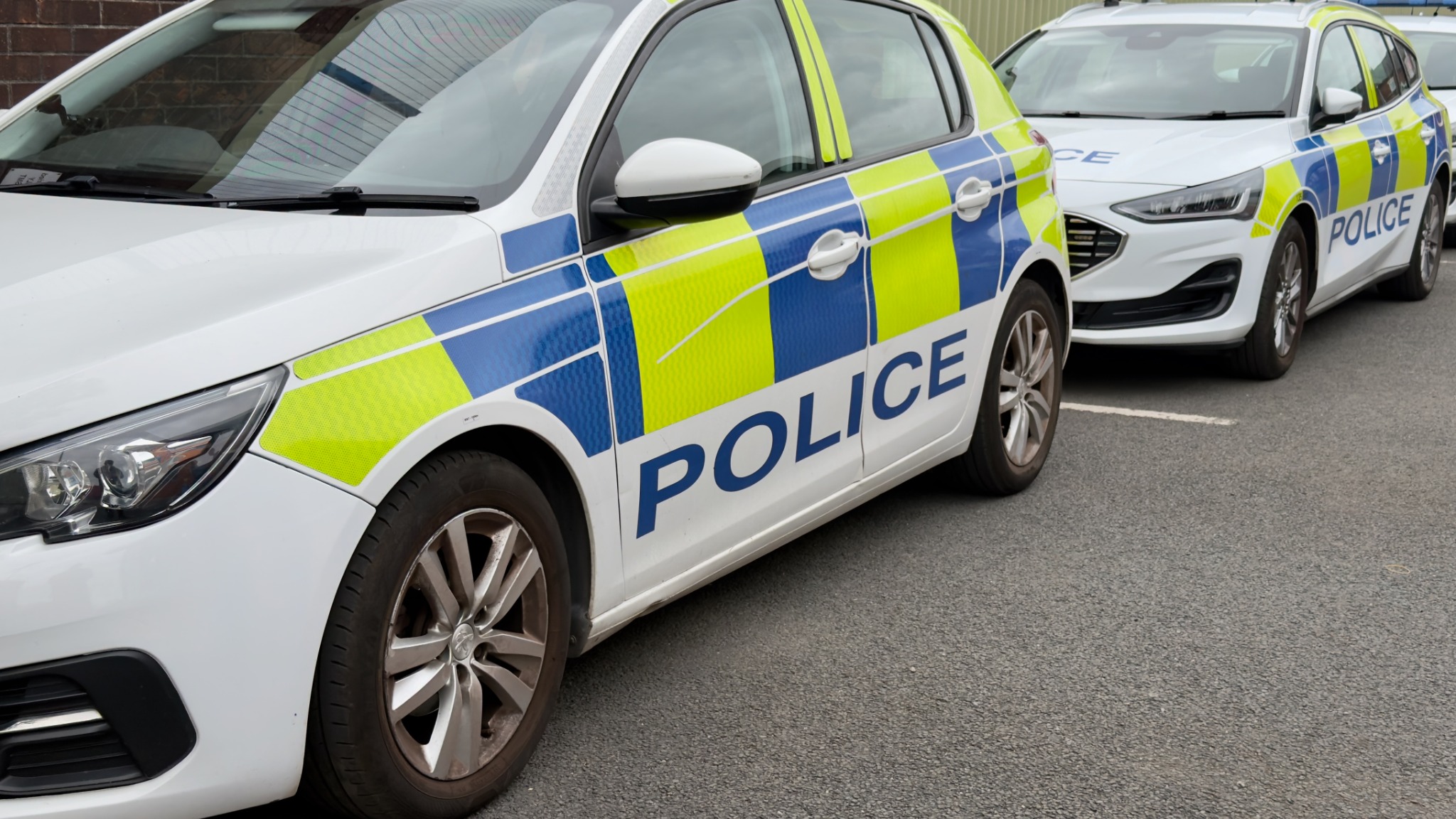 Two marked British police cars parked closely together, with blue and fluorescent yellow livery.